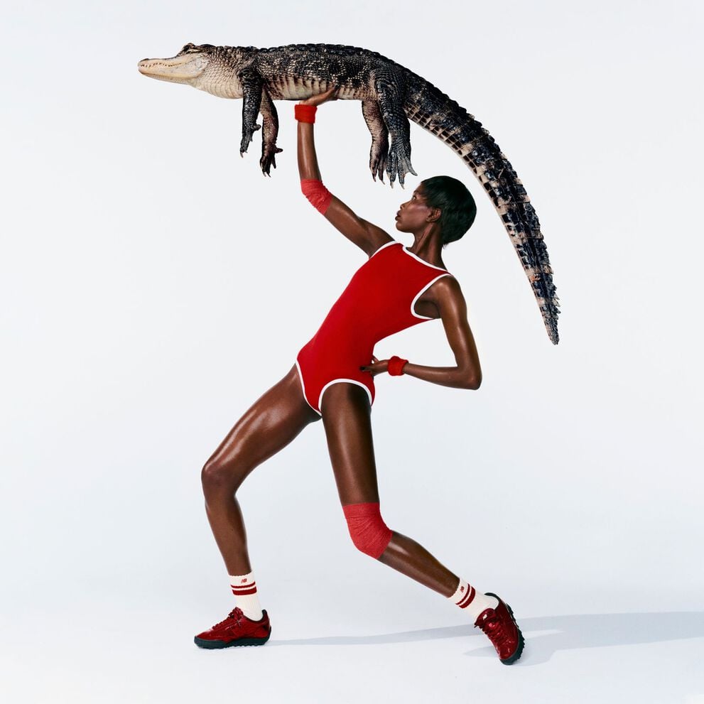 A woman in front of a white background wearing Gator Run shoes while holding an alligator